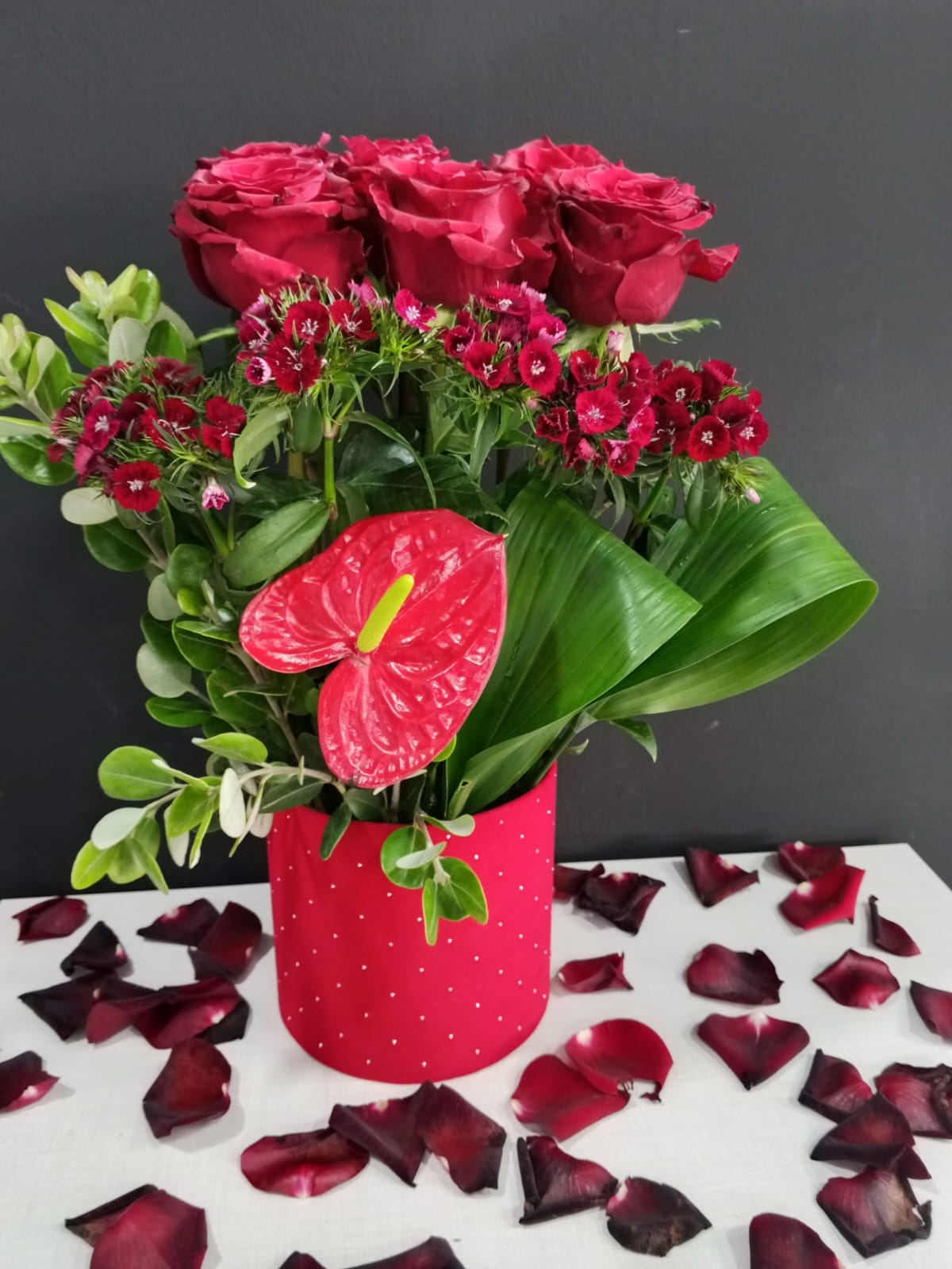 Red roses with anthurium and dianthus in red polka dot container
